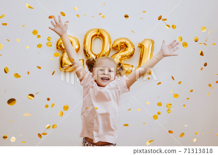 Little girl jumps, rejoices against, background of numbers 2021, confetti flies Little girl jumps, rejoices against, background of numbers 2021, confetti flies 71313818