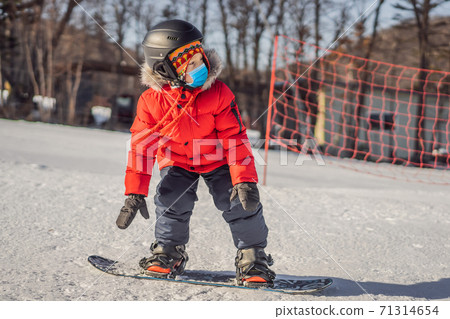 Little cute boy snowboarding wearing a medical mask during COVID-19 coronavirus. Activities for children in winter. Children's winter sport. Lifestyle 71314654