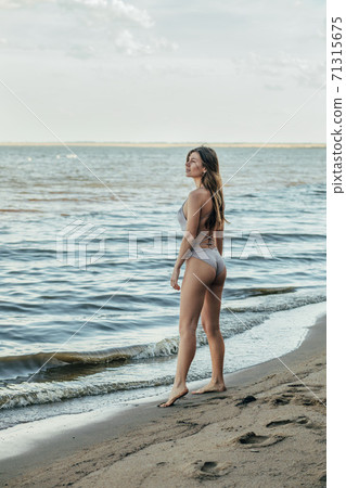 Portrait of a young beautiful woman in a beige swimsuit. Brown-haired woman walking on the beach. Portrait of a young beautiful woman in a beige swimsuit. Brown-haired woman walking on the beach. 71315675