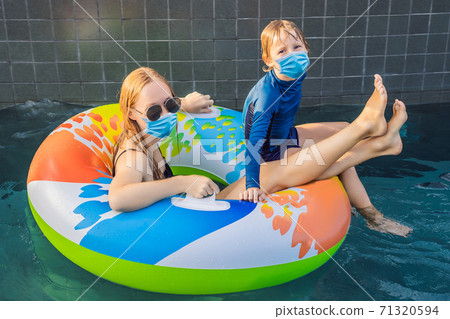 Mom and son wearing a medical mask during COVID-19 coronavirus have fun at the water park Mom and son wearing a medical mask during COVID-19 coronavirus have fun at the water park 71320594