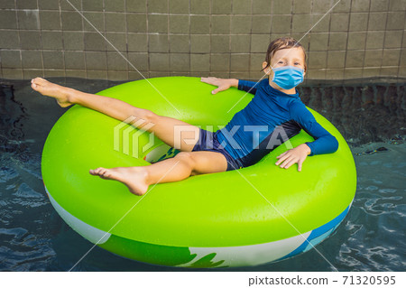 Little boy wearing a medical mask during COVID-19 coronavirus swimming with rubber ring at the leisure center Little boy wearing a medical mask during COVID-19 coronavirus swimming with rubber ring at the leisure center 71320595