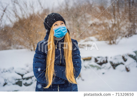 The woman wearing a medical mask during COVID-19 coronavirus was very froze in winter under snowfall. Winter problems The woman wearing a medical mask during COVID-19 coronavirus was very froze in winter under snowfall. Winter problems 71320650