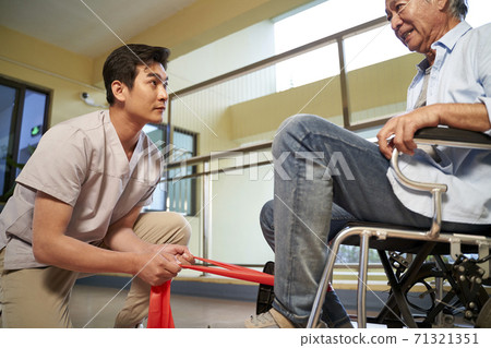 young asian physical therapist working with old man on enhancing leg strength using resistance band 71321351