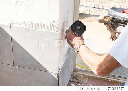 the mason prepares the wall with a chisel before laying a ceramic tile the mason prepares the wall with a chisel before laying a ceramic tile 71324371