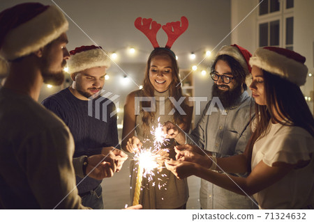 Group of young male and female friends stand in a circle and light sparklers on New Year's Eve. Group of young male and female friends stand in a circle and light sparklers on New Year's Eve. 71324632