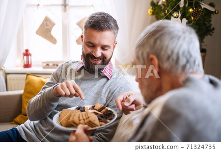 Mature man and senior father indoors at home at Christmas, eating biscuits. Mature man and senior father indoors at home at Christmas, eating biscuits. 71324735