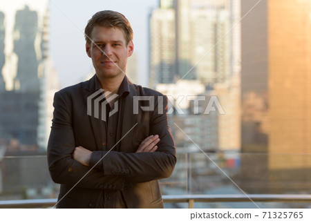 Young handsome businessman in suit with arms crossed against view of the city 71325765