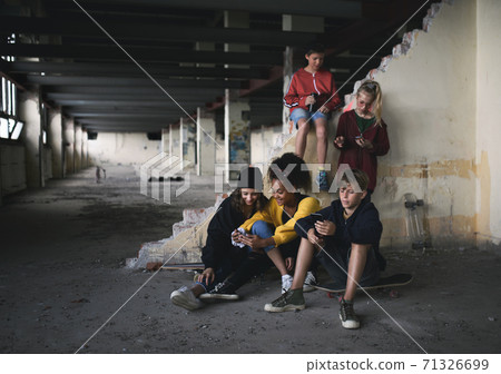 Group of teenagers gang sitting indoors in abandoned building, using smartphones. Group of teenagers gang sitting indoors in abandoned building, using smartphones. 71326699
