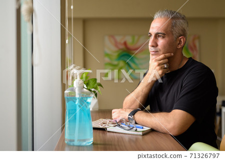 Handsome Persian man with gray hair thinking by window at the library 71326797