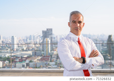 Handsome Persian businessman with arms crossed against view of the city 71326832