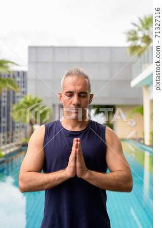 Mature Persian man meditating at the swimming pool on rooftop Mature Persian man meditating at the swimming pool on rooftop 71327116