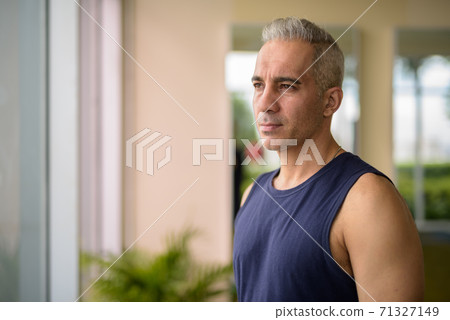 Mature handsome Persian man thinking by window at the gym 71327149