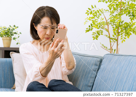 A woman looking at a smartphone with reading glasses 71327397