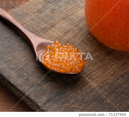 red caviar in a wooden brown spoon on the table, behind a full jar of caviar red caviar in a wooden brown spoon on the table, behind a full jar of caviar 71327404