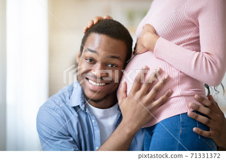 Handsome black man listening his wife's pregnant belly at home Handsome black man listening his wife's pregnant belly at home 71331372