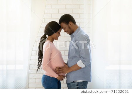 Handsome black man touching his pregnant wife's belly indoors, side view Handsome black man touching his pregnant wife's belly indoors, side view 71332061