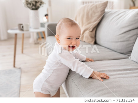 Cute Little Baby Smiling To Camera Standing Near Couch Indoor 71332154
