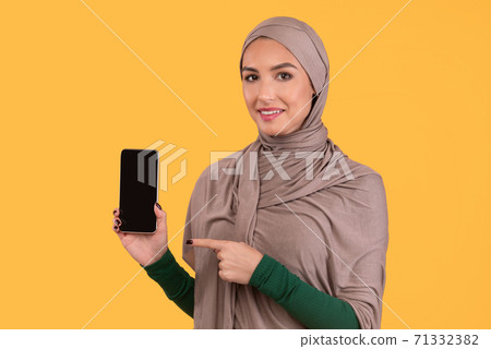Muslim Lady Pointing At Smartphone Screen Posing On Yellow Background 71332382