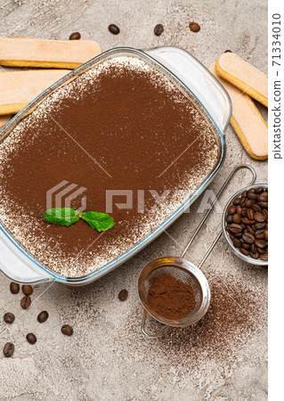 Traditional Italian Tiramisu dessert in glass baking dish and savoiardi cookies on concrete background Traditional Italian Tiramisu dessert in glass baking dish and savoiardi cookies on concrete background 71334010