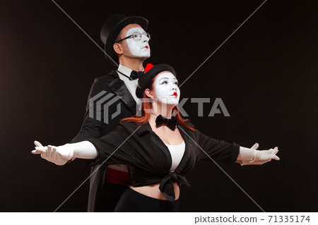 Portrait of two mime artists performing, isolated on black background. Man is standing behind the woman holding her hands. Portrait of two mime artists performing, isolated on black background. Man is standing behind the woman holding her hands. 71335174