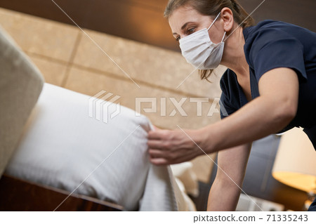 Chambermaid in protective mask is doing room service in hotel 71335243