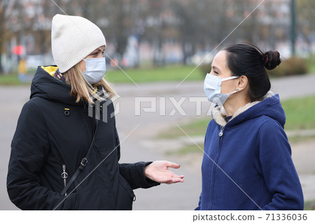 Two women in medical protective masks communicate in street. Two women in medical protective masks communicate in street. 71336036