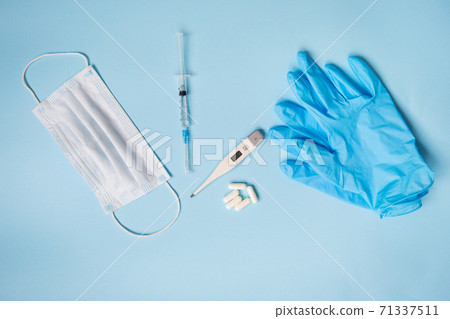 Blue latex gloves on a blue background lie with pills, medical mask, thermometer and syringe. The concept of health and self-control for viruses and epidemics. Close-up Blue latex gloves on a blue background lie with pills, medical mask, thermometer and syringe. The concept of health and self-control for viruses and epidemics. Close-up 71337511