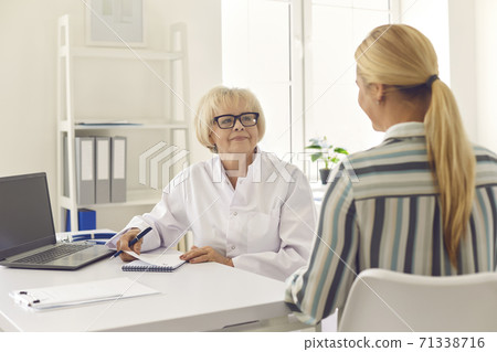 Senior doctor prescribing treatment for young woman during check-up in modern clinic 71338716