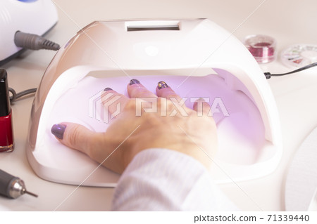 A girl's hand in an ultraviolet nail lamp with nail polish files 71339440