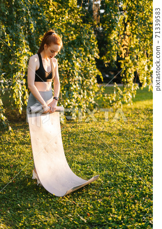 Attractive fitness young woman rolling up yoga mat finishing performing yoga exercising. 71339583