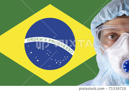 Man close-up in white protective suit, mask, glasses and gloves on the background of the flag of Brazil, coronavirus pandemic threat. Epidemic, pandemic of coronavirus covid-19. Doctor in respirator. 71339728