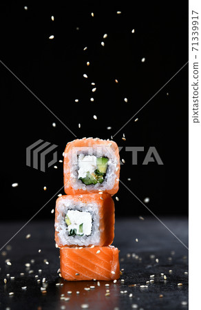 Japanese and Asian cuisine sushi set rolls Philadelphia with fresh salmon ingredients over black background with text copy space and sesame falling down 71339917