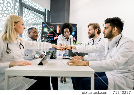 Successful meeting, teamwork concept. Multiracial healthcare experts, doctors, coordinating, stacking their hands together, while having a meeting at modern clinic 71340257