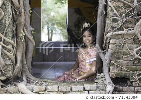 A Thai girl in traditional Thai dress sits inside an old church of an old Thai temple. 71343394