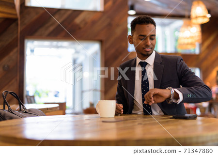 Businessman sitting and checking time from his watch in coffee shop Businessman sitting and checking time from his watch in coffee shop 71347880