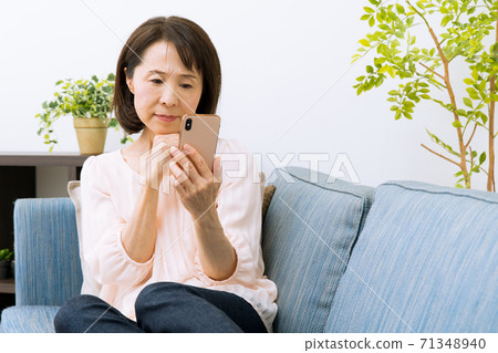 A woman looking at a smartphone is surprised and troubled 71348940