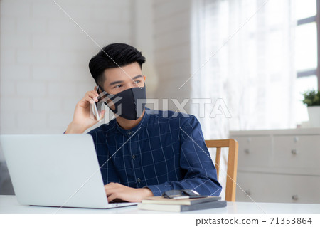 Young asian business man in face mask talking smartphone and work on laptop computer. 71353864