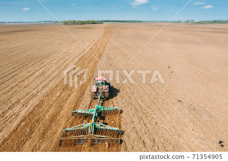 Aerial View. Tractor Plowing Field In Spring Season. Beginning Of Agricultural Spring Season. Cultivator Pulled By A Tractor In Countryside Rural Field Landscape Aerial View. Tractor Plowing Field In Spring Season. Beginning Of Agricultural Spring Season. Cultivator Pulled By A Tractor In Countryside Rural Field Landscape 71354905