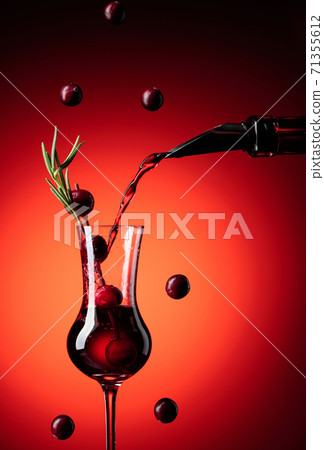 Cranberry liquor is poured from a bottle into a glass. 71355612