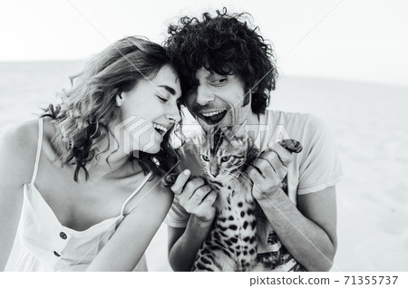 A handsome man with curly hair gently hugs his beloved. They have a cat in their hands A handsome man with curly hair gently hugs his beloved. They have a cat in their hands 71355737