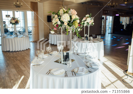 Luxurious restaurant. Luxurious interior, white tables, serving dishes and glasses for guests Luxurious restaurant. Luxurious interior, white tables, serving dishes and glasses for guests 71355866