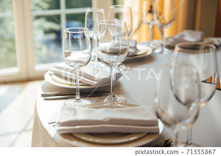 Luxurious restaurant. Luxurious interior, white tables, serving dishes and glasses for guests Luxurious restaurant. Luxurious interior, white tables, serving dishes and glasses for guests 71355867
