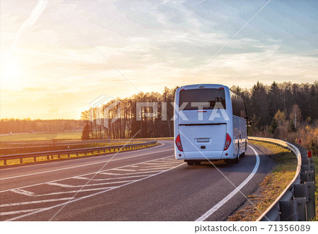 A passenger bus travels along the highway against the backdrop of a forest and a sunset in the sky. Passenger transportation concept, safety and comfort, copy space for text 71356089