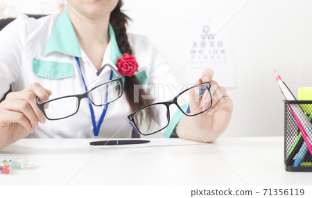 Doctor ophthalmologist holds in his hands two glasses for the eyes. The concept of choosing the right and comfortable modern glasses, copy space Doctor ophthalmologist holds in his hands two glasses for the eyes. The concept of choosing the right and comfortable modern glasses, copy space 71356119