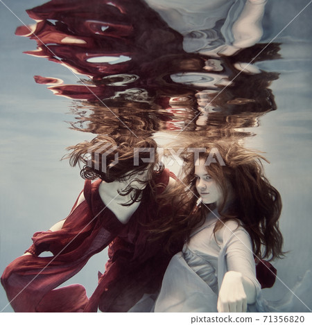 Two girls underwater in blue and red dresses with developing long hair seem to fly in weightlessness and interact with each other Two girls underwater in blue and red dresses with developing long hair seem to fly in weightlessness and interact with each other 71356820