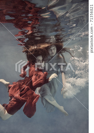 Two girls underwater in blue and red dresses with developing long hair seem to fly in weightlessness and interact with each other Two girls underwater in blue and red dresses with developing long hair seem to fly in weightlessness and interact with each other 71356821