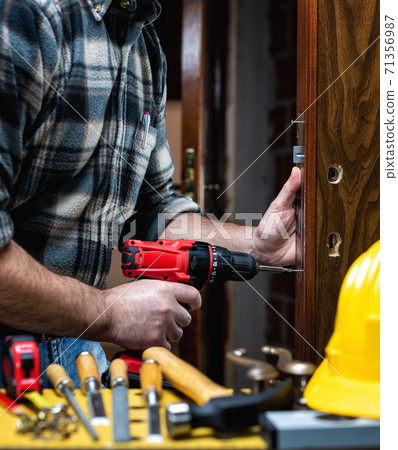 Carpenter at work repairs and installs the door lock. Carpentry. 71356987