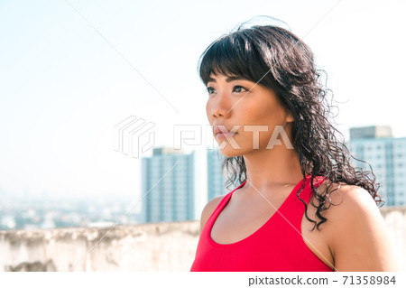 Young Asian woman looking far distance into the skyline buildings at rooftops. Female athelete determined in sport outfit with copy space 71358984