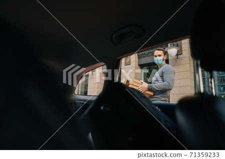 Shooting from interior car of delivery man wearing medical protective mask holding boxes with pizza. 71359233