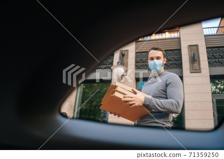 Shooting from interior car of delivery man wearing medical protective mask holding boxes with pizza. Shooting from interior car of delivery man wearing medical protective mask holding boxes with pizza. 71359250